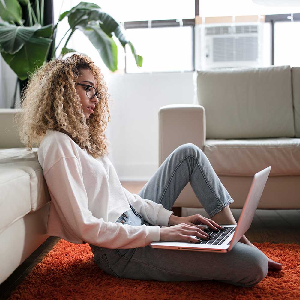 woman sitting on red carpet in living room with latop