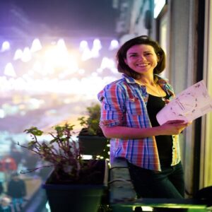 Woman standing and leaning against the balcony holding a flyer with vibrant nightlife background