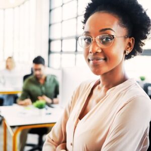 Coloured woman smiling in an office with people behind her | Build Self-Esteem at Work