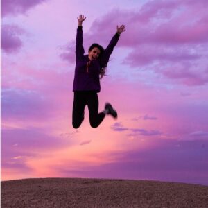 Woman jumping in the air in joy with beautiful purple sky background