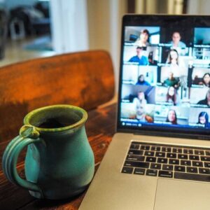 Coffee mug placed on a table next to a laptop displaying a video call with many people in it