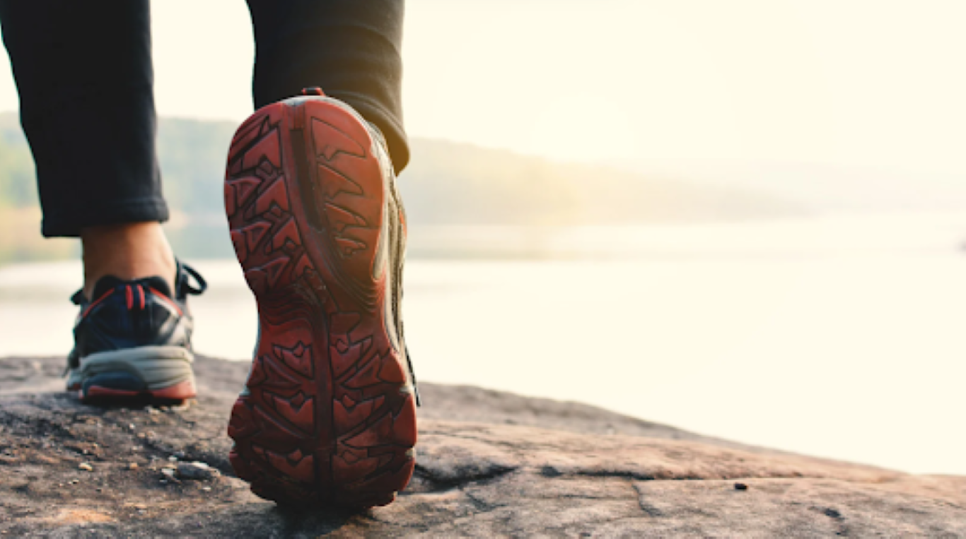 Close-up of a person’s running shoe on a rocky trail with a sunlit background, symbolizing forward movement, momentum, and outdoor team connection.
