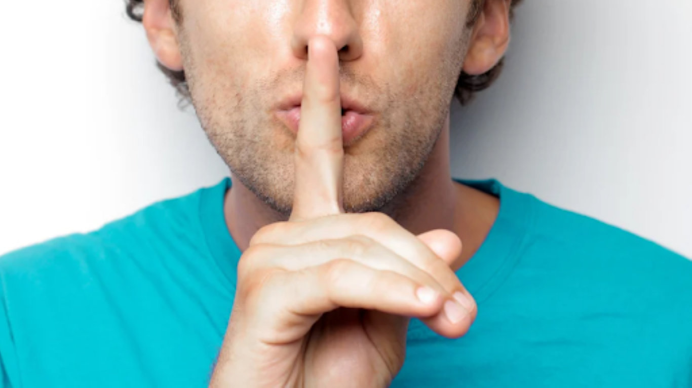 Close-up of a person with their finger held to their lips in a playful “shhh” gesture, symbolizing a fun secret or surprise. Image promotes a story about unexpected team-building experiences that create deep connection without pressure.