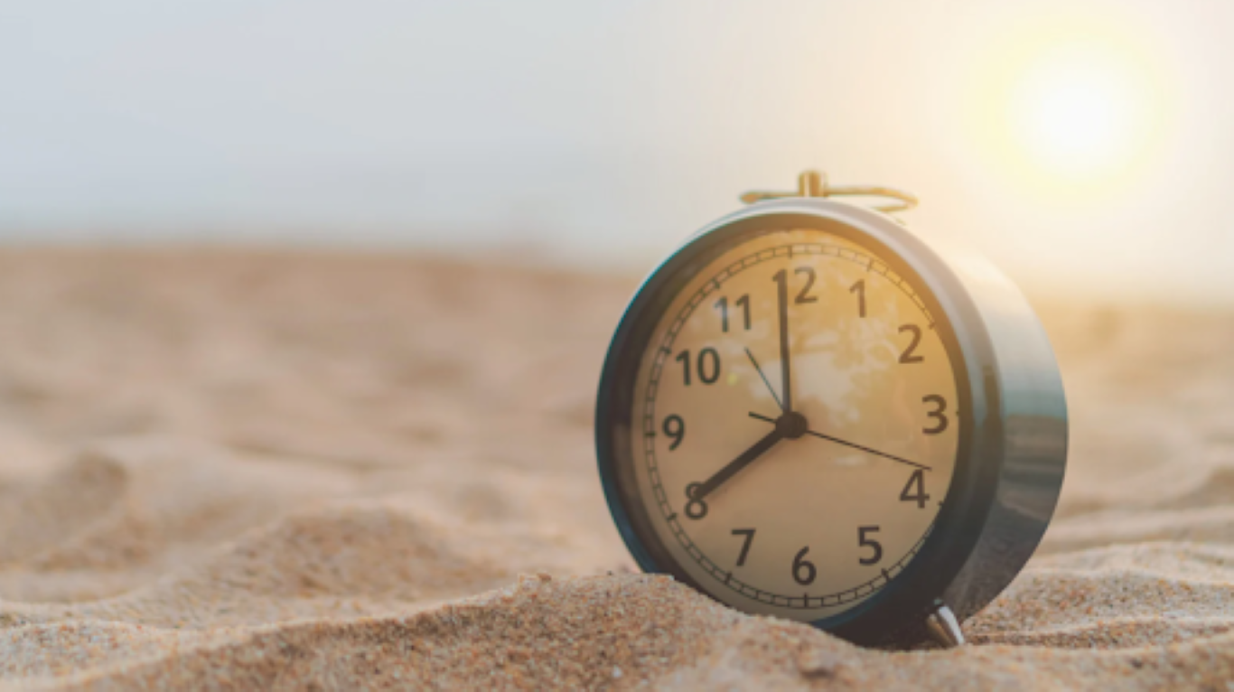 Un réveil posé sur le sable au lever du soleil, symbolisant la puissance d’une heure intentionnelle pour retrouver clarté, leadership et élan d’équipe.