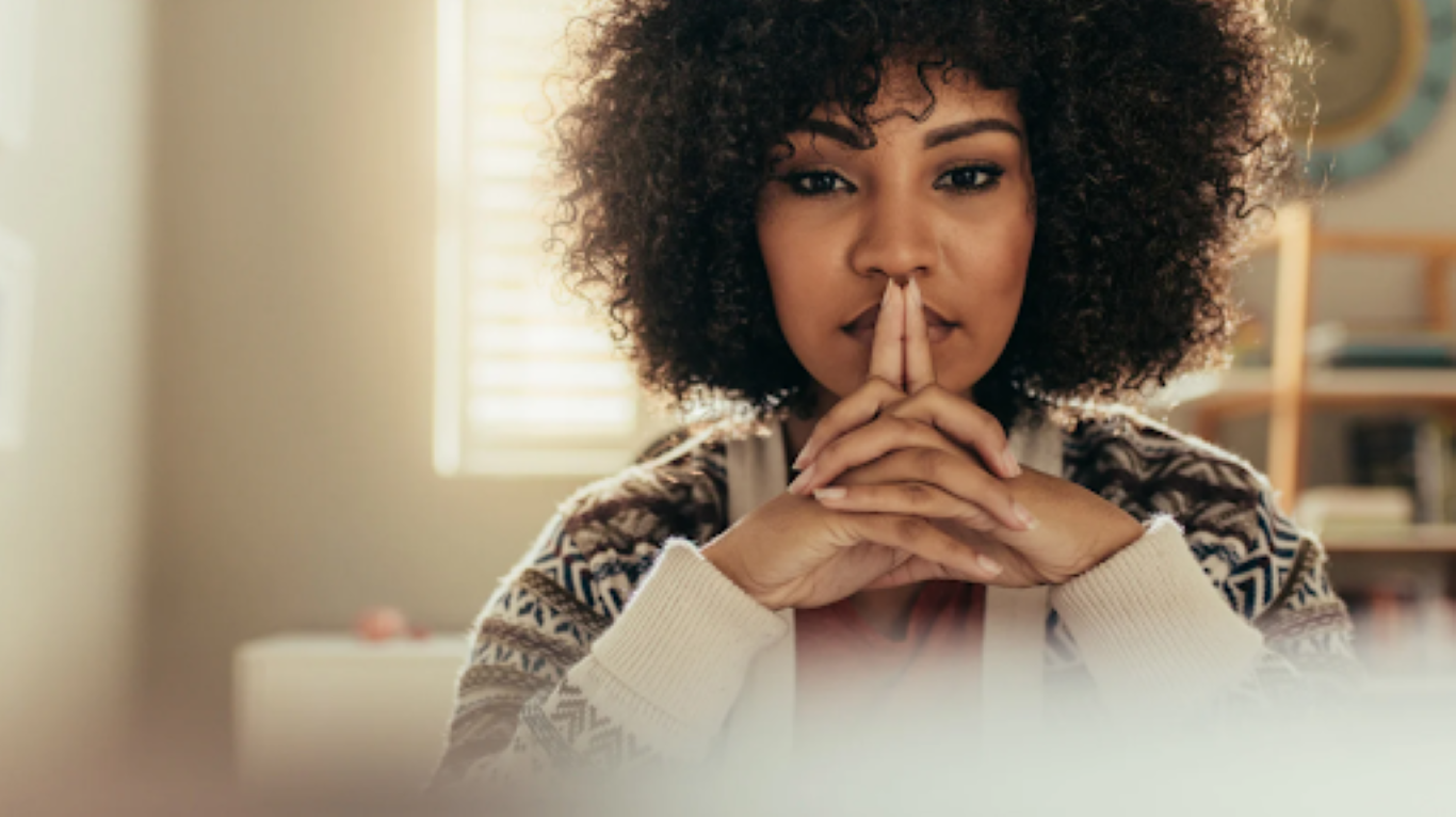 Femme pensive regardant droit devant elle, les doigts croisés devant la bouche, représentant la réflexion intérieure et le dialogue mental des leaders sous pression.