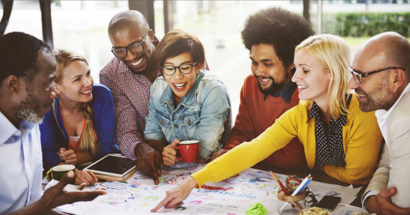 A diverse team of professionals smiling and brainstorming together around a colorful table during a creative collaboration session, symbolizing trust, autonomy, and authentic teamwork.