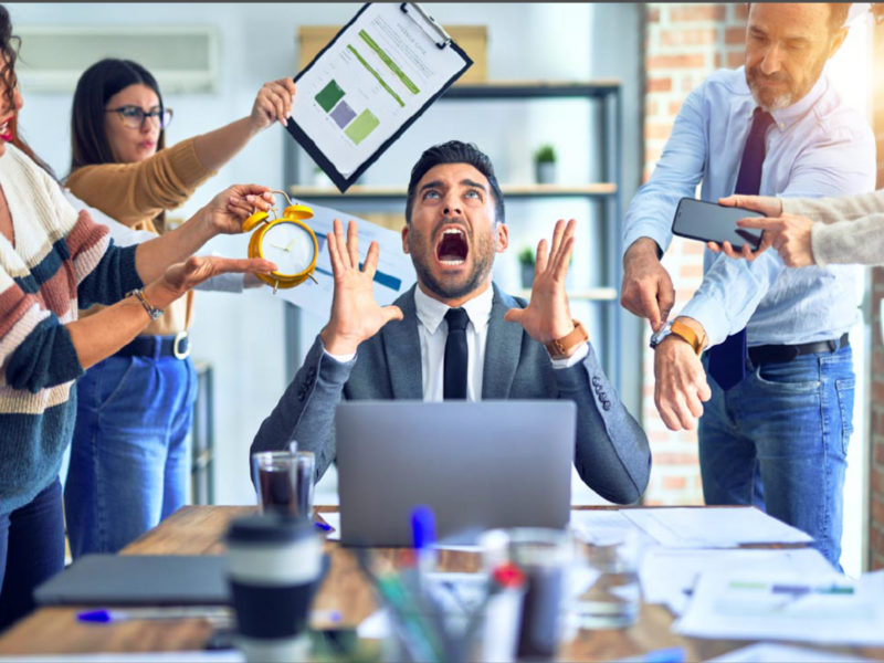 Leader overwhelmed at a desk while team members demand attention, illustrating decision pressure, urgency, and leadership stress.