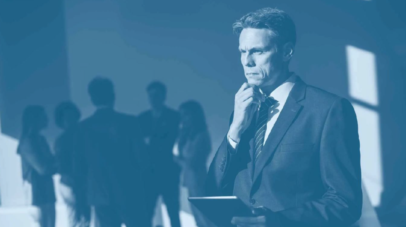 Leader pensif avec une tablette, sous pression, pendant que l’équipe apparaît floue en arrière-plan.