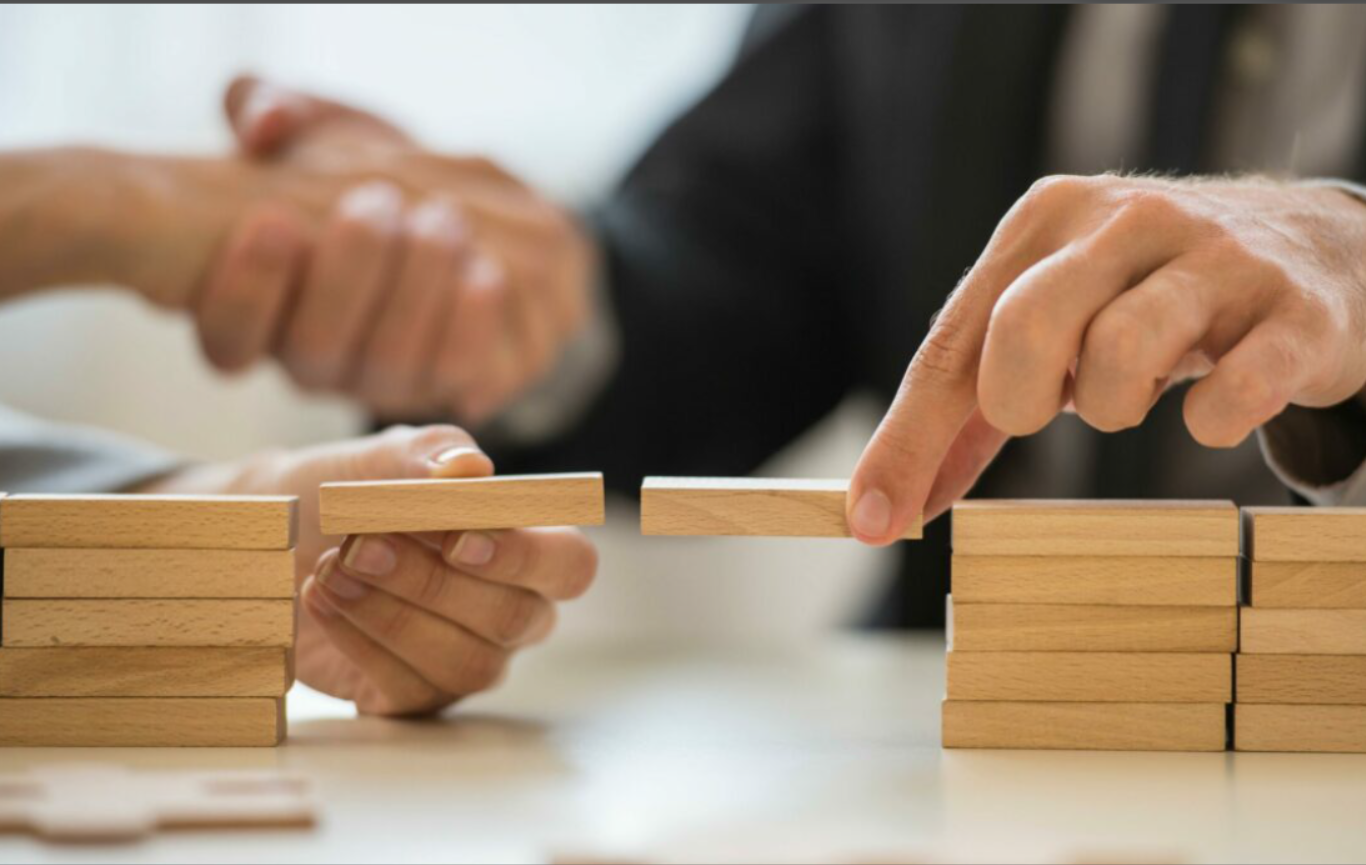 Hands carefully placing a wooden block bridge between two stacks, symbolizing trust, psychological safety, and connection built through leadership presence.